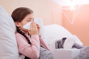 Little tired ill child sneezing with her eyes closed while leaning on a pillow